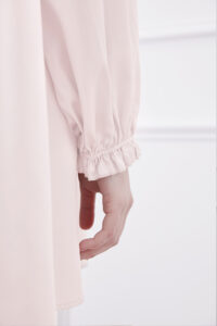 Close-up of woman in ballet pink silk mini dress showcasing detailed ruffle trim at lantern sleeves cuff.