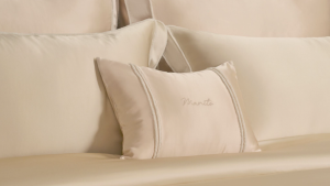 Champagne silk bedding with matching pillows and a decorative MANITO embroidered cushion.